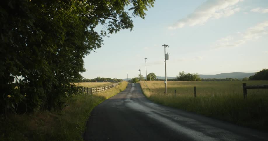 A wet dirt road goes through large fenced fields