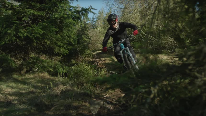 A cyclist rides down a bumpy hill in the woods
