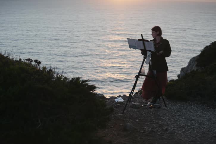A young person is painting outside by the ocean in the middle of the day