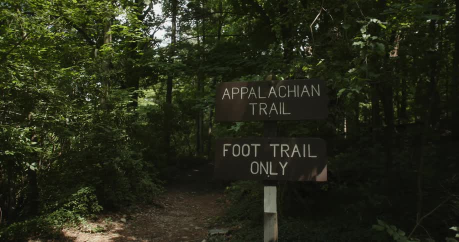 A sign beside a hiking trail through a woodland during the day