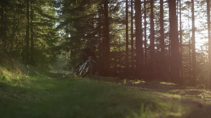 There is a young white man riding his bike in the middle of the forest