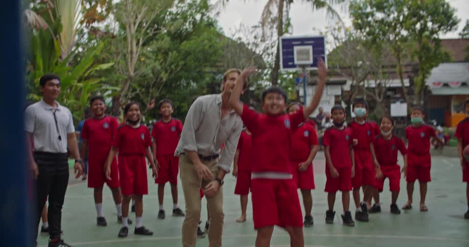 Other kids laugh and smile while they watch one of them attempt a basketball shot