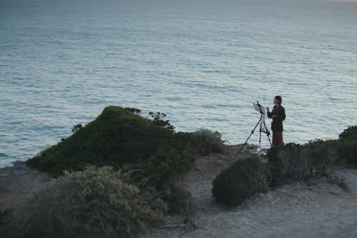 A woman is painting by the shore