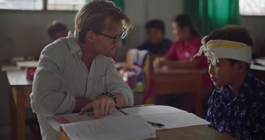 A teacher instructs a student on the contents of a textbook in a classroom during the day
