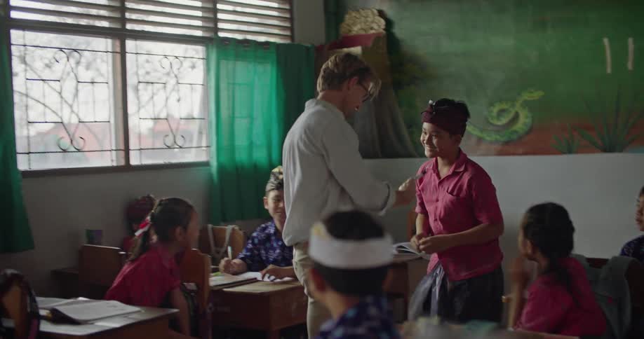 A teacher walks to the front of the class with a student