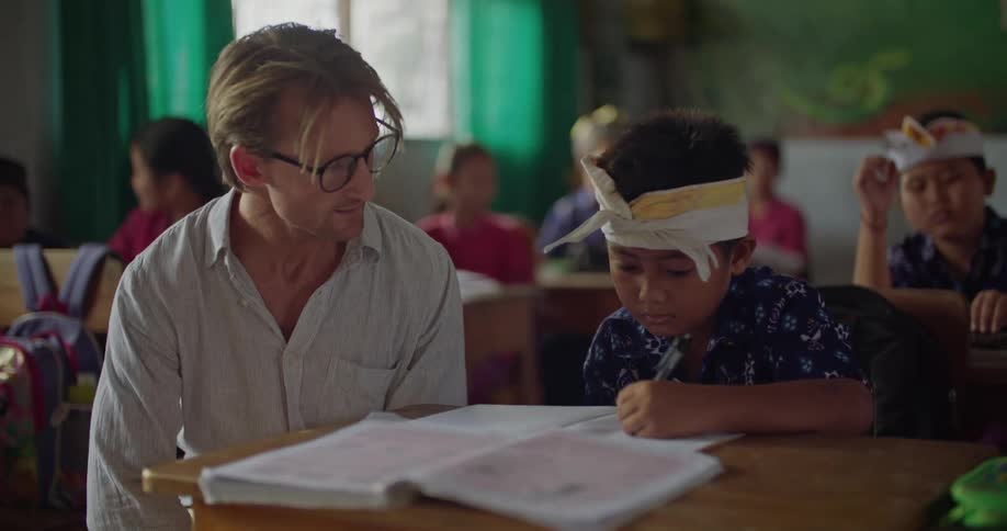 A teacher is sitting with a student in aclassroom of kids