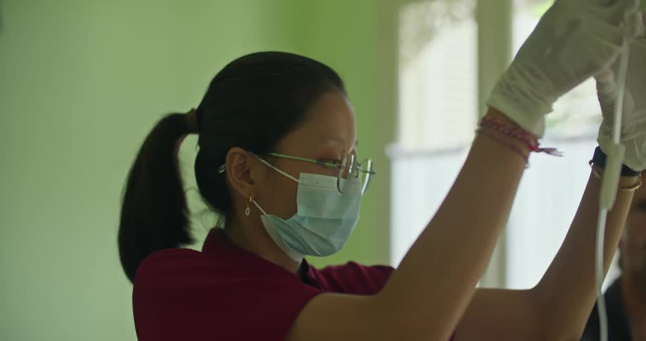 Man watches as nurse wearing face mask injects solution into iv