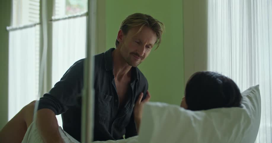 A man sits with his wife in bed in the hospital