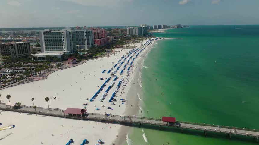 Drone follows the shoreline of a beach in Florida, with tourists sunbathing under umbrellas
