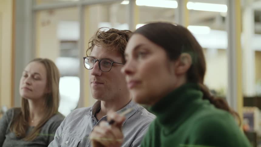 Two women and a man in a classroom with a wall and window in the background