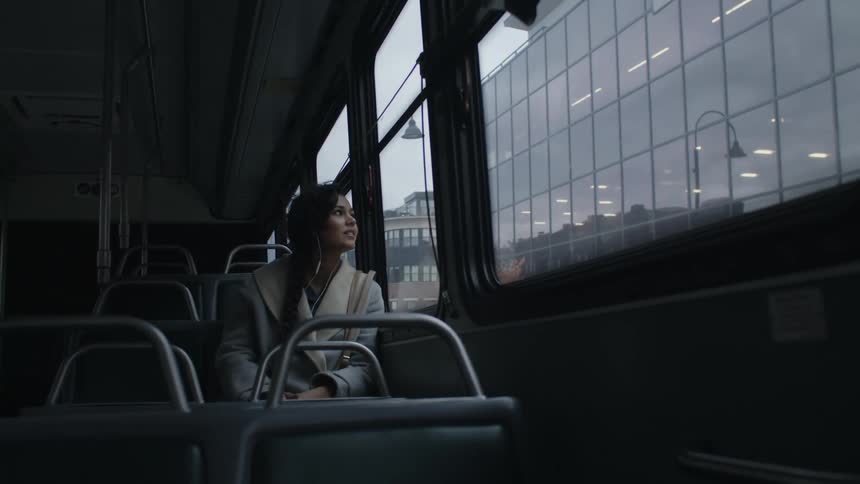 A woman sits on a train and looks out the window to the city building