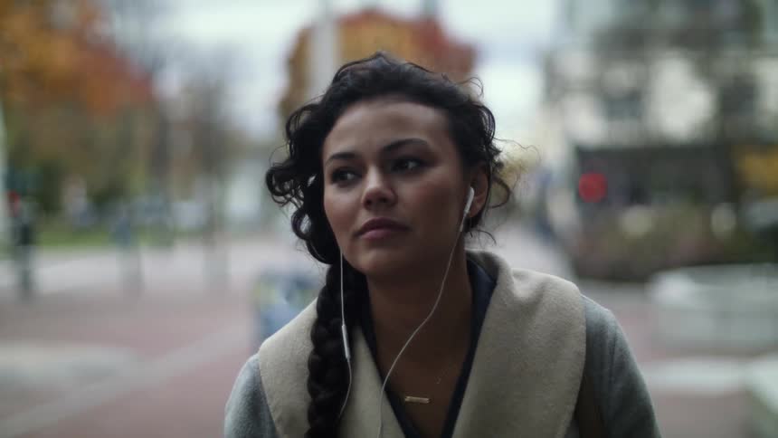 A woman is walking down a city street as her hair moves in the wind