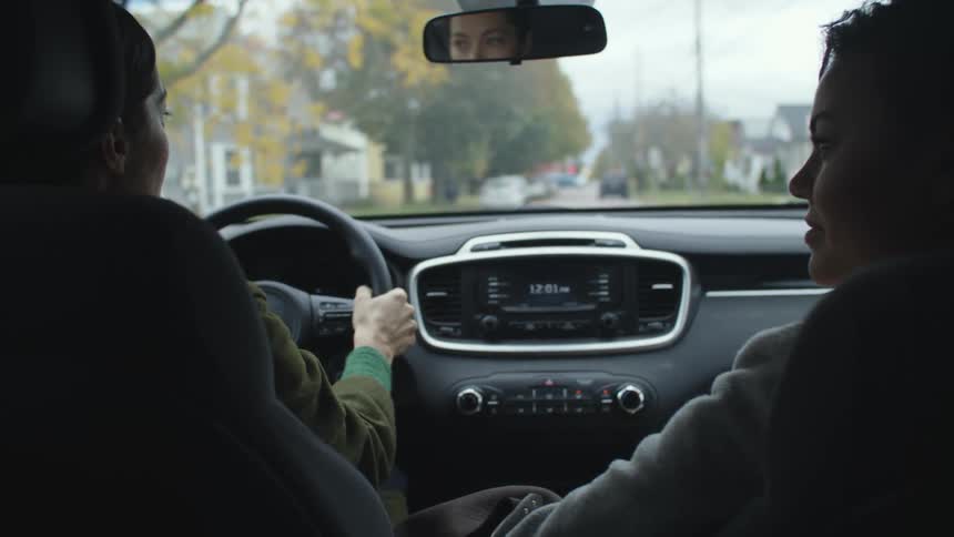 Two women talk while driving along road through neighborhood as leaves start to change color