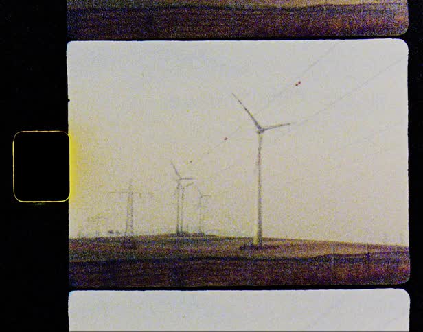Spinning wind turbine over a hill caught on vintage film from a moving vehicle