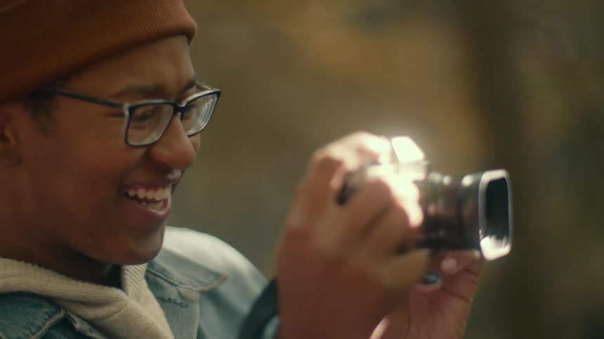 Happy man wearing glasses talks while taking pictures with a vintage camera outdoors