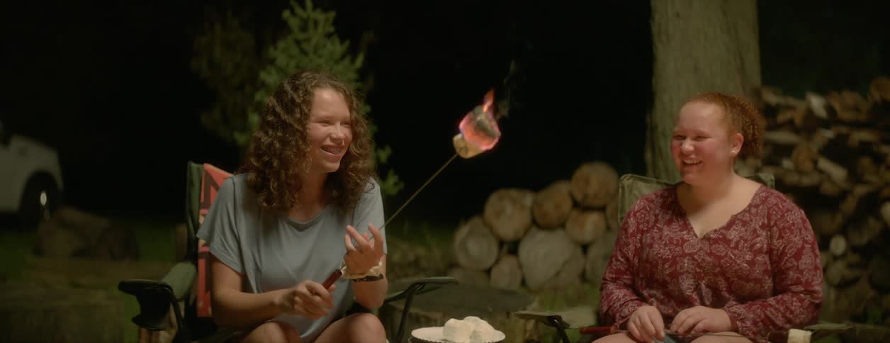 A view of three people sitting outdoors cooking marshmallows