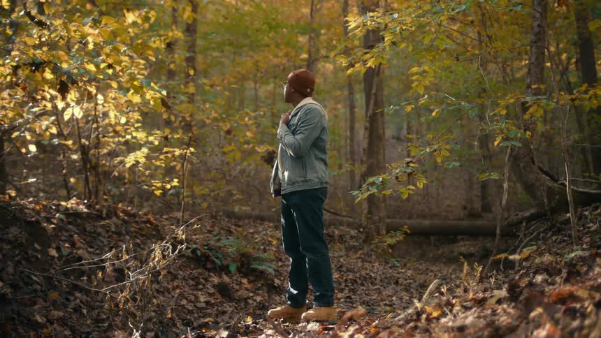 There is a young black man standing in the middle of the forest
