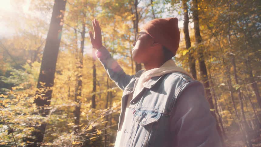 Young man standing in the forest covers his eyes with his hands while facing the bright sun