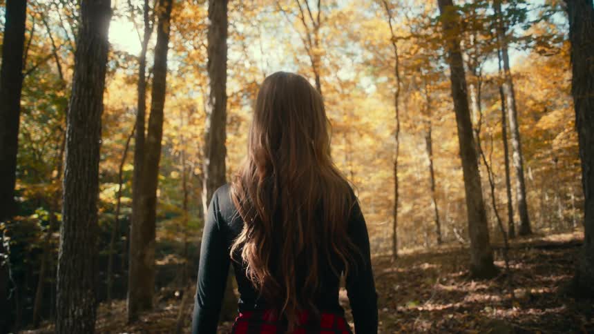There is a young white woman that is walking outside in the forest area