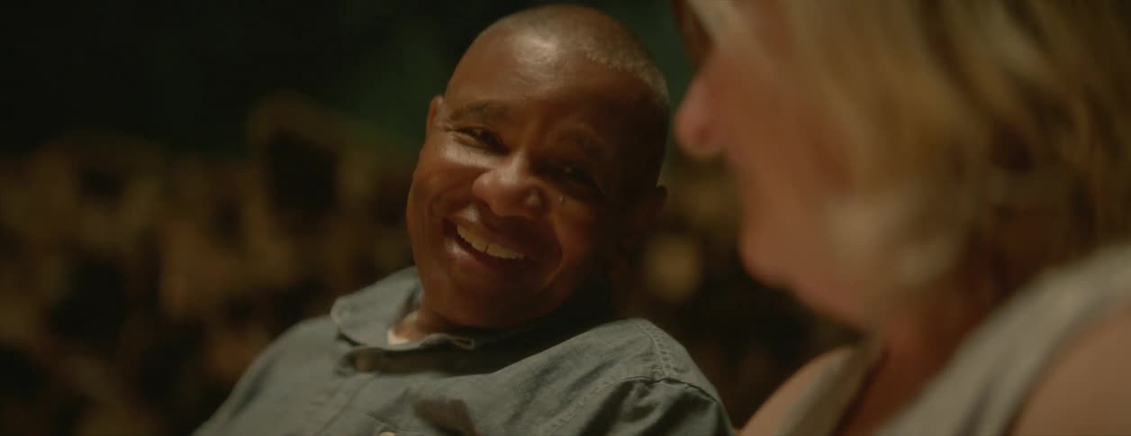 A mature man kisses the hand of his wife while sitting near a campfire at night
