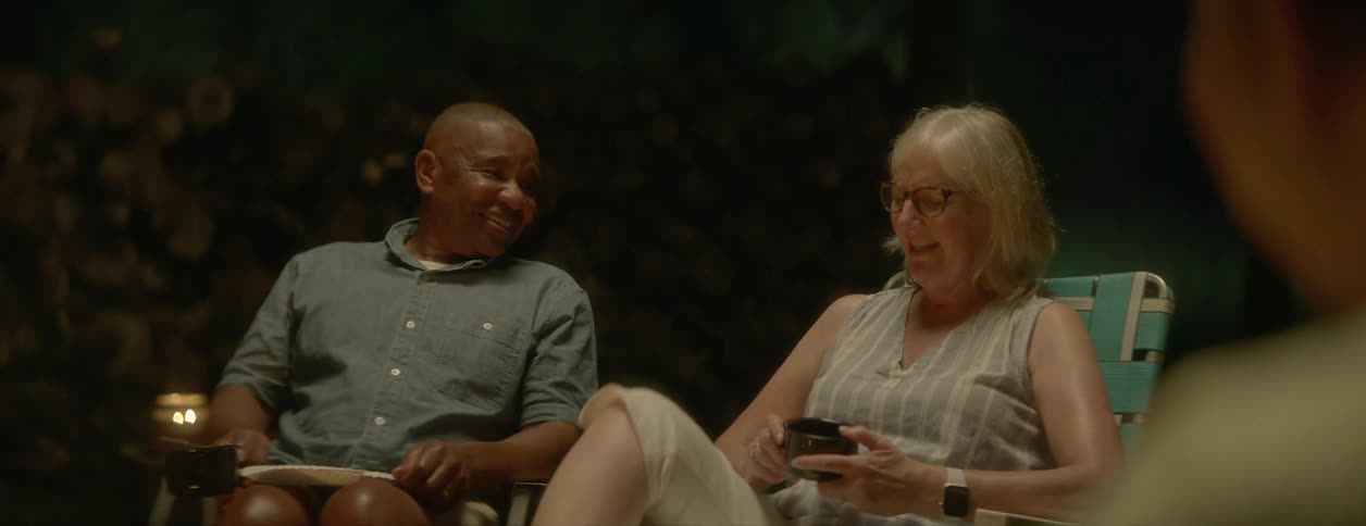 A relaxed mature couple sitting outdoors on a campfire talk to each other