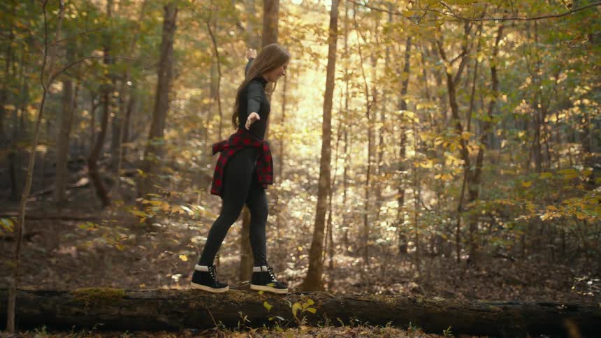 Young woman walks balancing over a fallen tree in the forest at morning