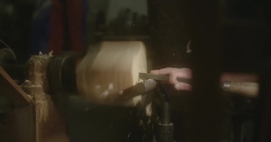 A person carves a spinning piece of wood using a woodworking lathe
