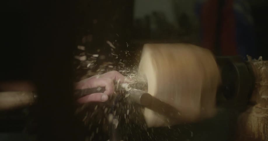 A man feeds a metal tube into a block of wood on a rotating saw