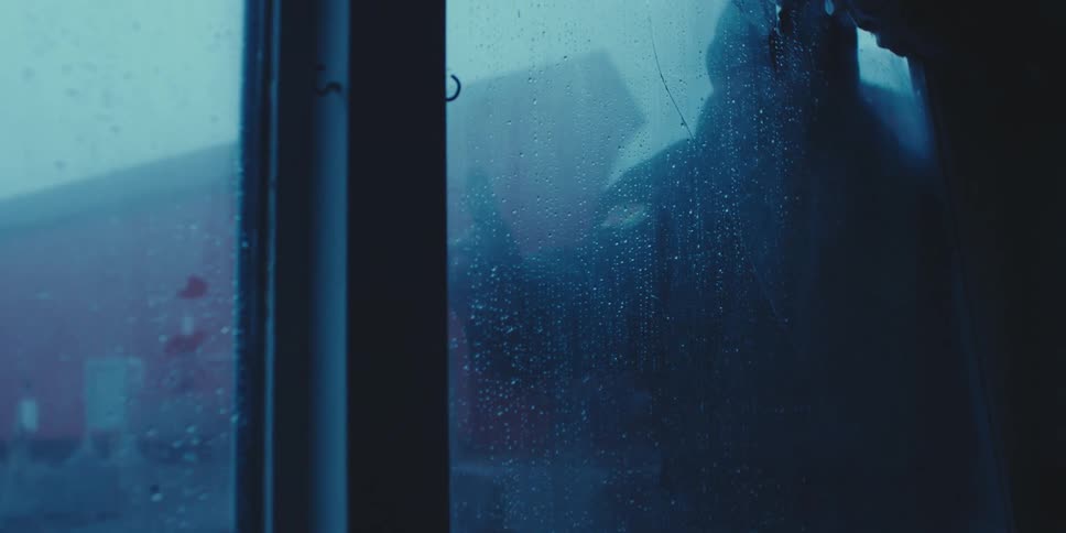 Person wearing jacket with patch on jacket knocks on wet glass of building and gestures
