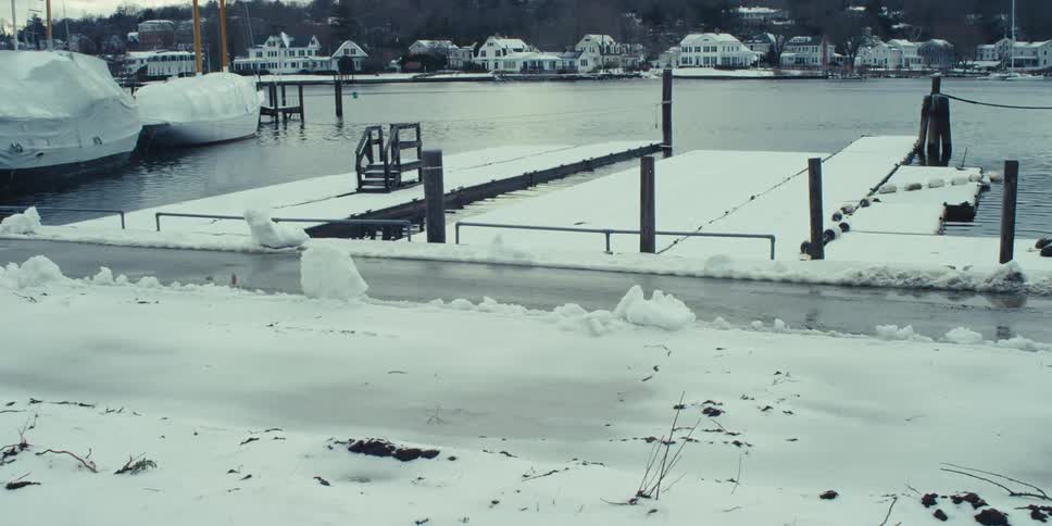 Snow covered wooden docks in the water across from homes and next to tarped boats