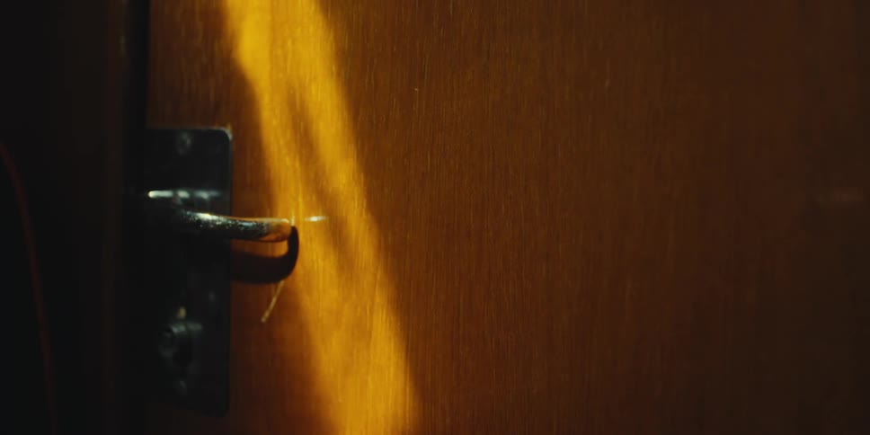Light moves across a wooden door and the door handle in a dimly lit room