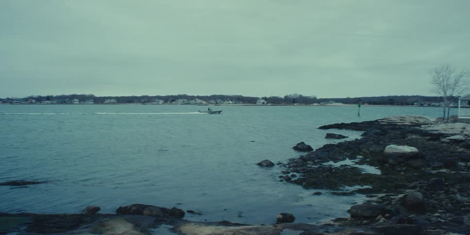 People on a motorboat traveling past a house on the shore with windows shuttered