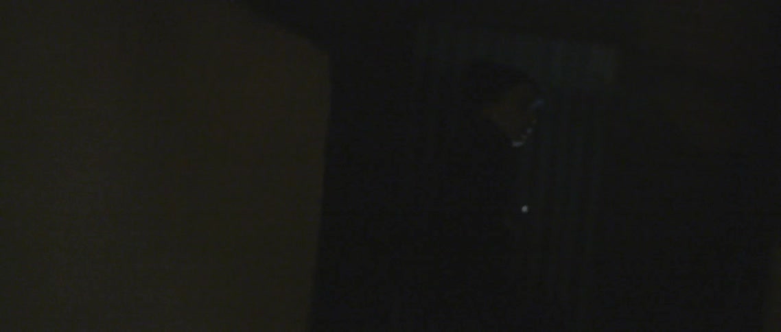 A boy runs to a building and puts the flash light on his face