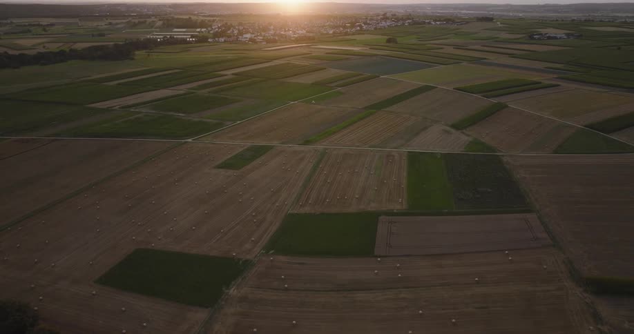 The sun glows on the horizon highlighting a town and a patchwork of farm fields