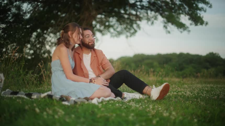 A couple kiss while sitting on a blanket under a tree
