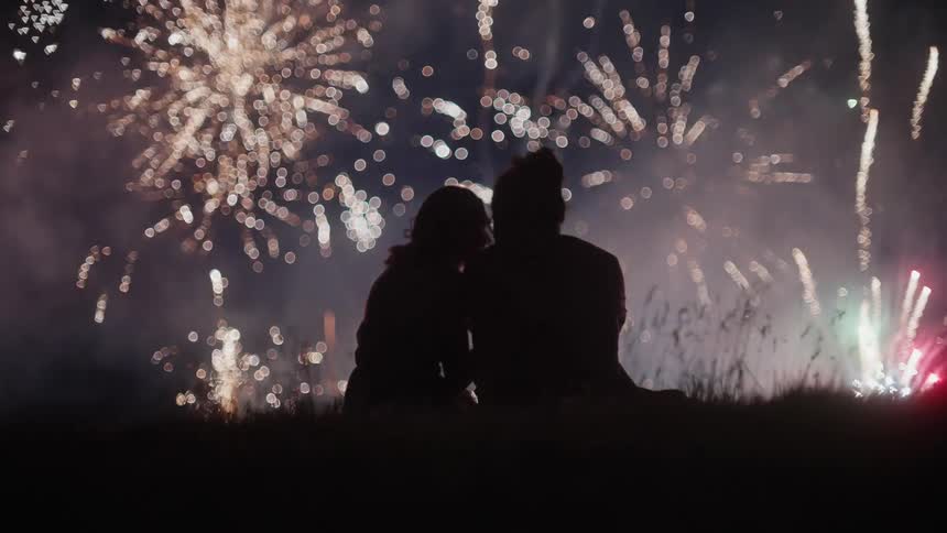 A woman leans on her partners shoulder while watching a fireworks show