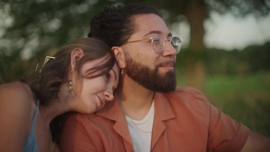 A woman puts her head on her boyfriends shoulder as they sit in the grass