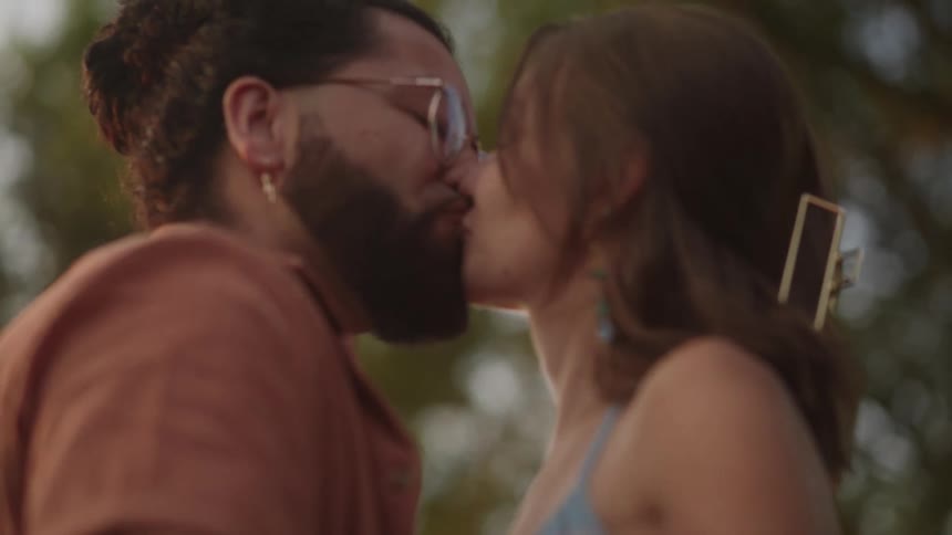 A man and a woman are standing outside holding hands and looking into each others eyes and they kiss