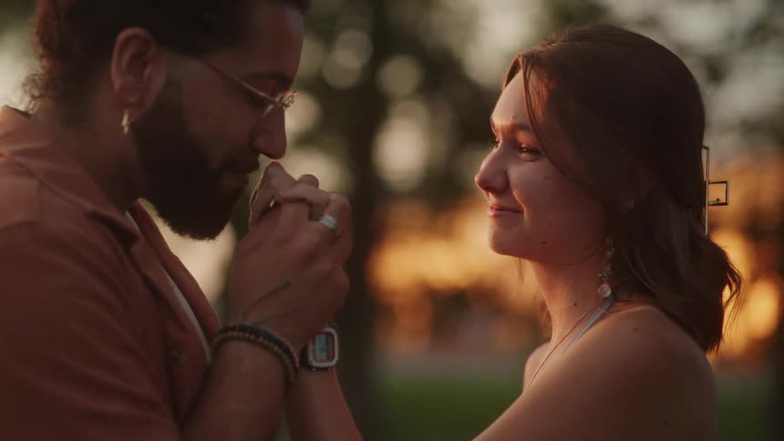 A woman smiles and laughs as her boyfriend kisses her hand