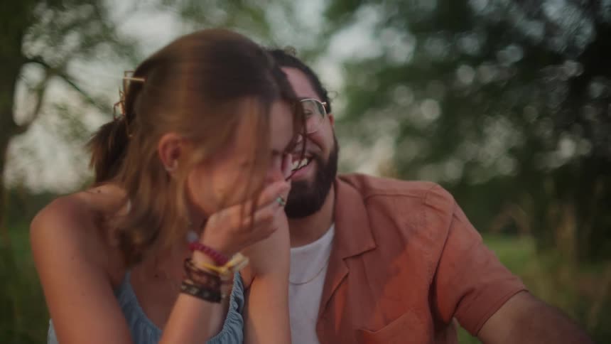 A man leans on a womans shoulder and they laugh as they sit outside