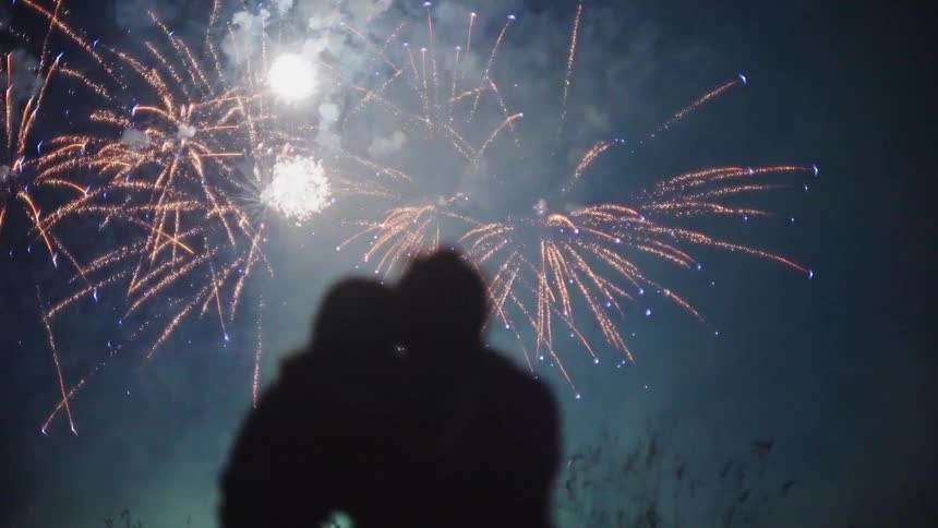 A woman rests her head on her partners shoulder during a fireworks show