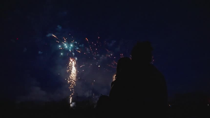 A couple sits close together as numerous magnificent fireworks explode overhead
