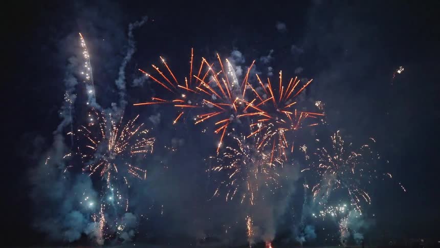 The silhouette of a couple sitting in the grass watching fireworks bursting in the night sky
