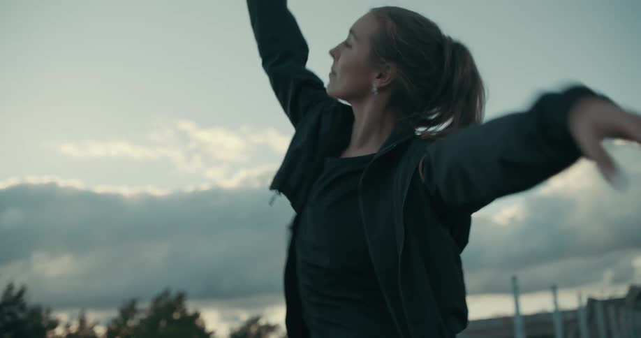 A woman and a man are outside with their arms in the air as they dance under a cloudy sky