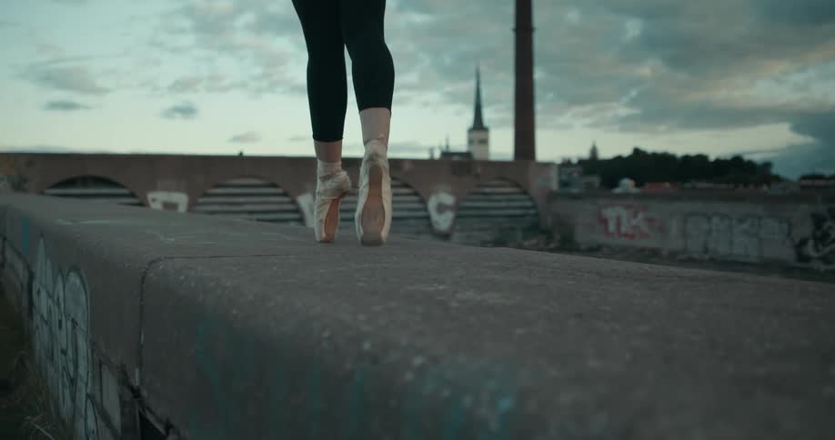 Ballerina balances on toe shoes while moving along concrete wall covered with graffiti