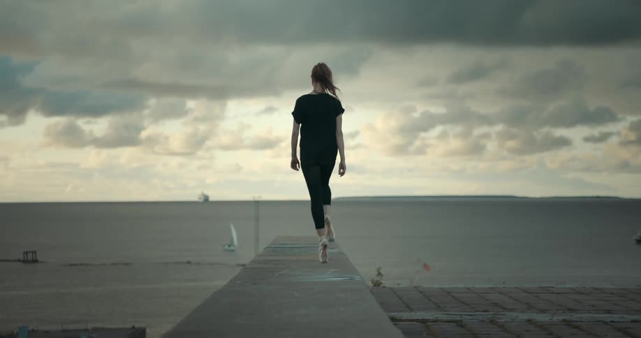 A ballet dancer walks en pointe along a ledge on the beach