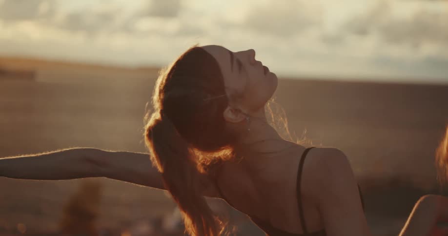 Young woman with hair blowing in the wind posing in front of the ocean at sunset