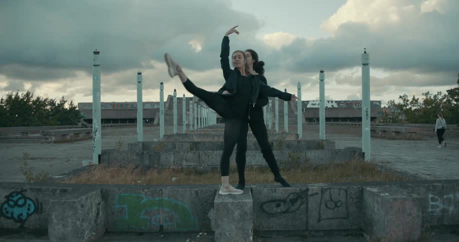 Ballet dancers move dance slowly on graffiti covered low wall as pedestrians walk in the background