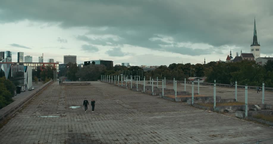 People are walking through a cobblestone park and there are tall city buildings in the distance