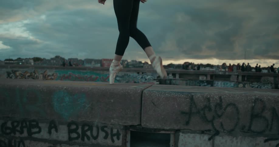A ballet dancer walks on her toes on a ledge